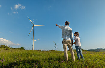 Grüner Wasserstoff von Westfalen. Vater und Sohn stehen in Wiese vor Windkraftanlage